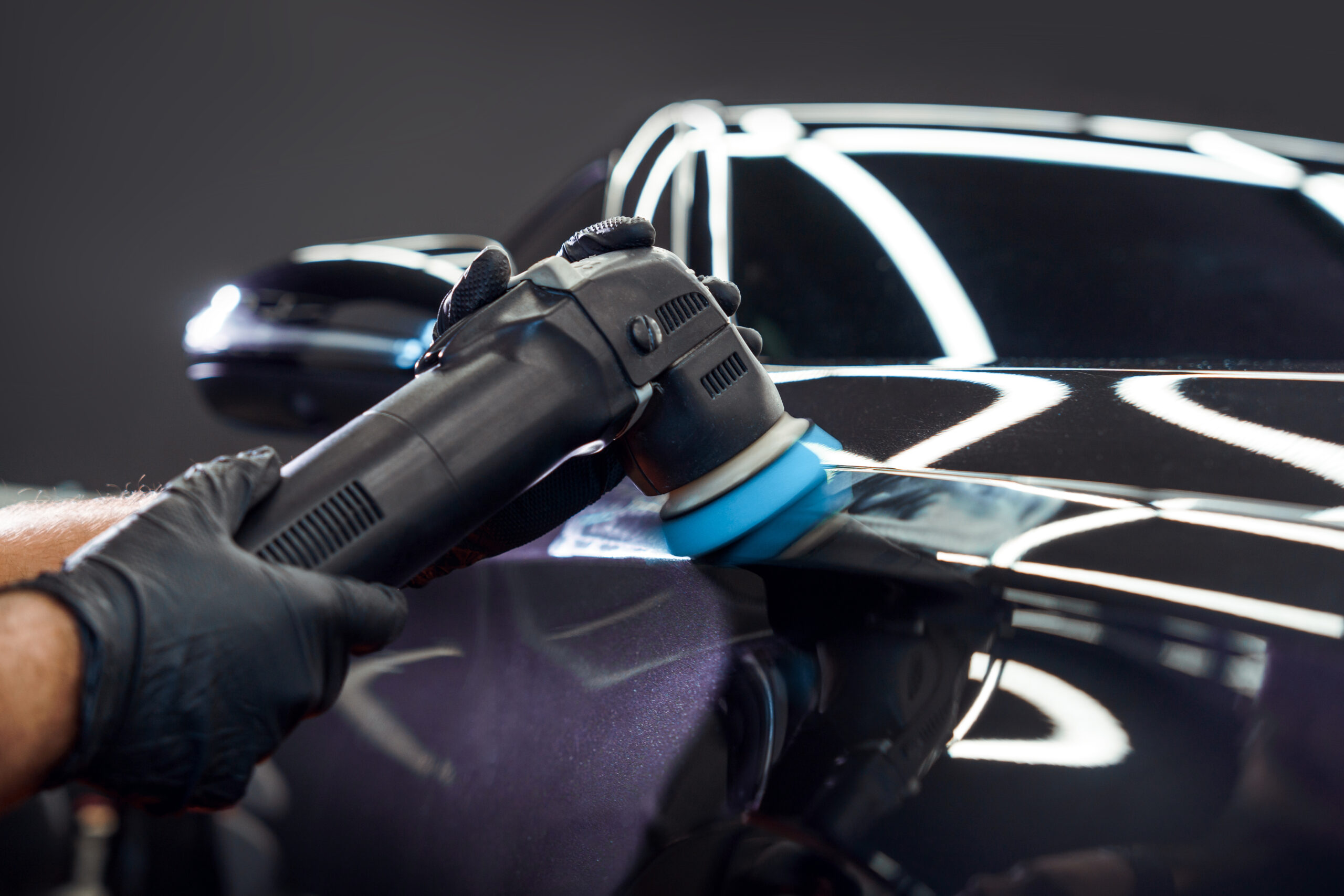 Car detailing and polishing. The hands of a professional car service worker, with an orbital polisher, polishing the hood of a car in a car service center