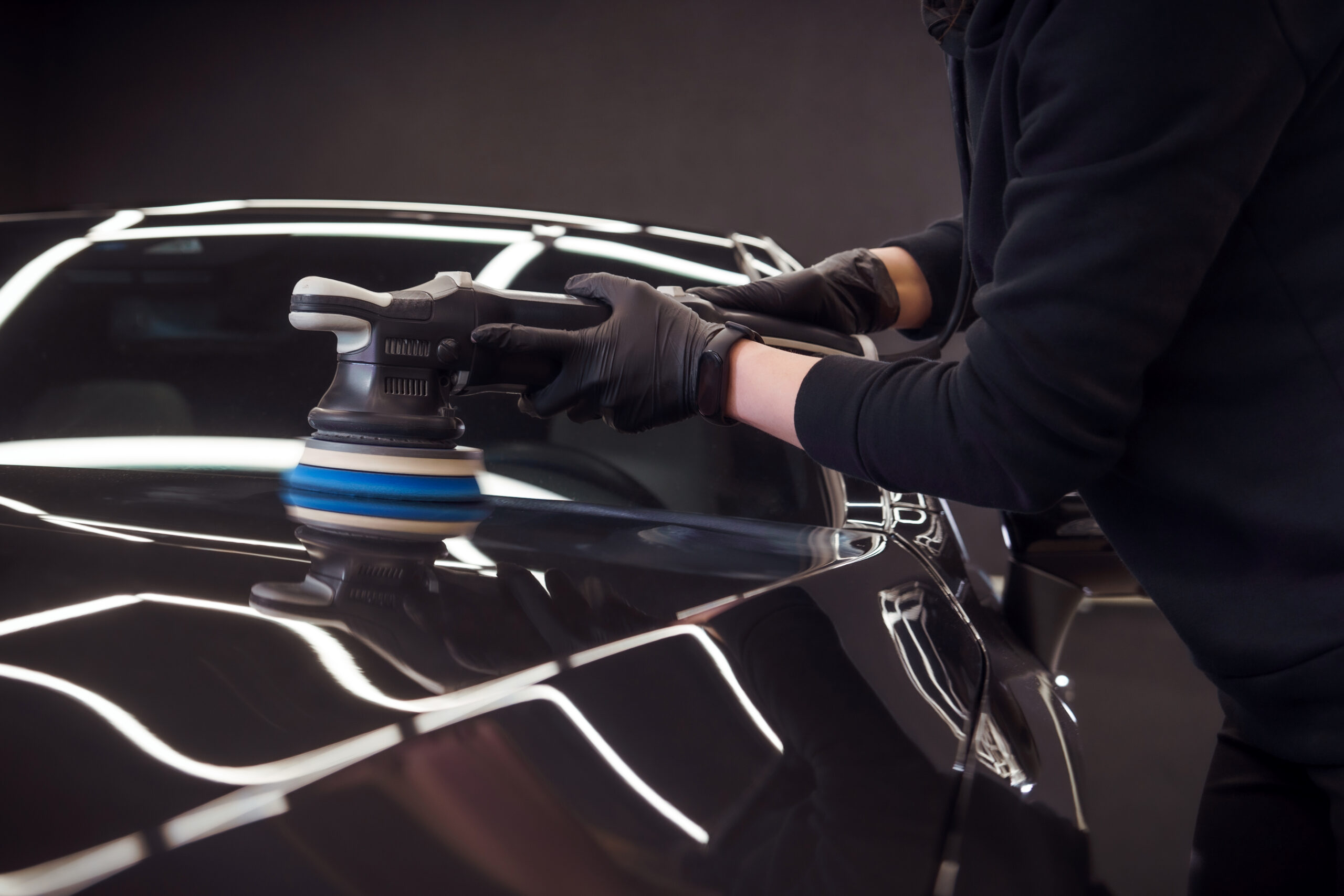 Car detailing and polishing. The hands of a professional car service worker, with an orbital polisher, polishing the hood of a car in a car service center