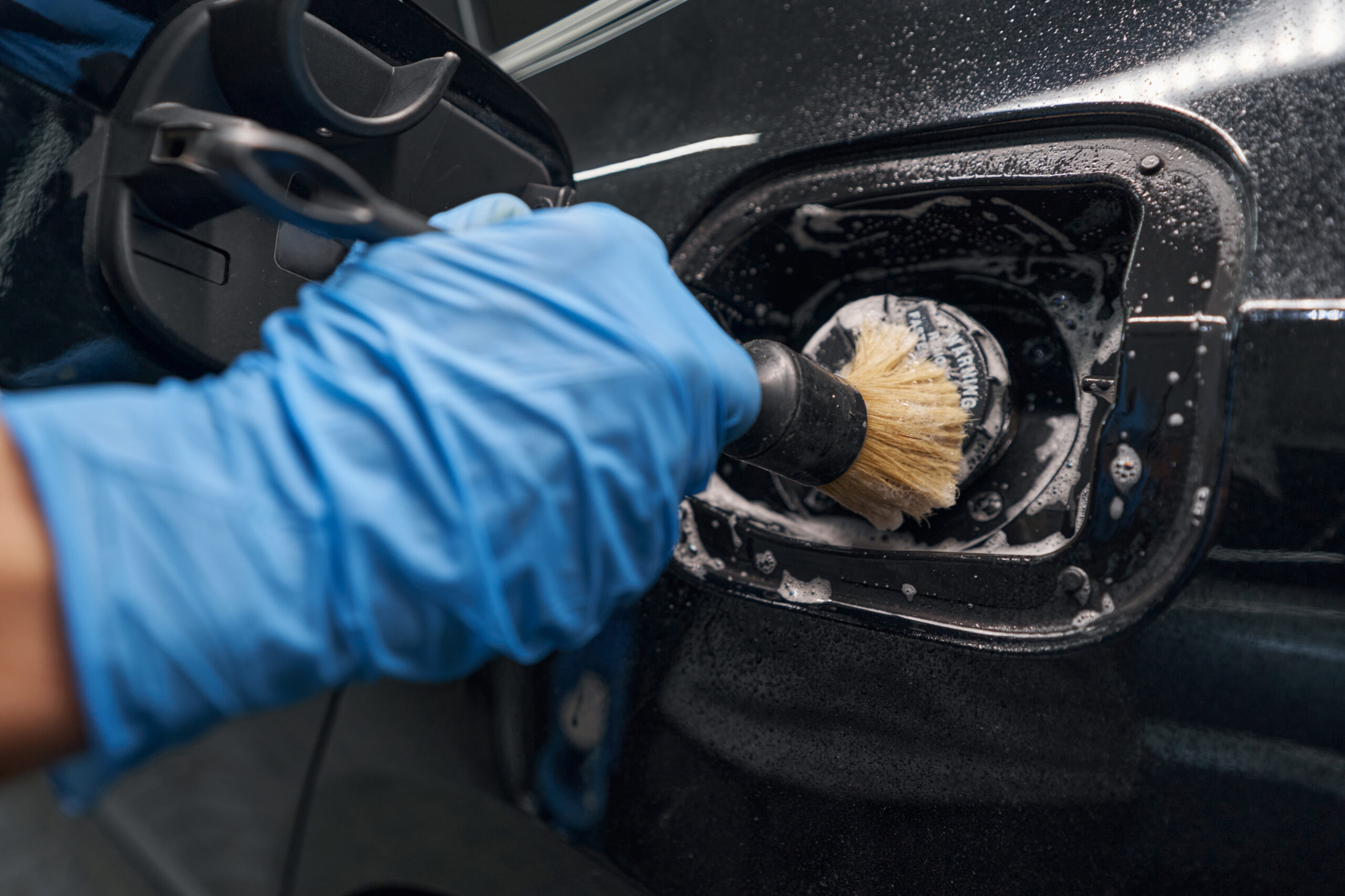 Close up of hand in protective glove carefully detailing and cleaning car with washing detergent and brush